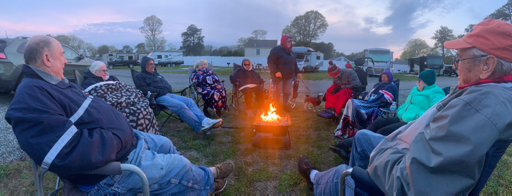 Group of people gathered near RV and a campfire at sunset